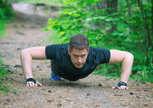 Handsome man doing push-ups in the forest. - Photo, Image