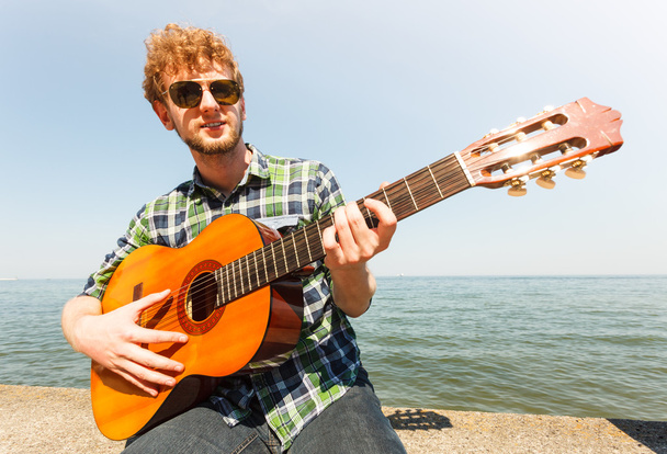 Young man hipster playing guitar by sea ocean. - Фото, изображение