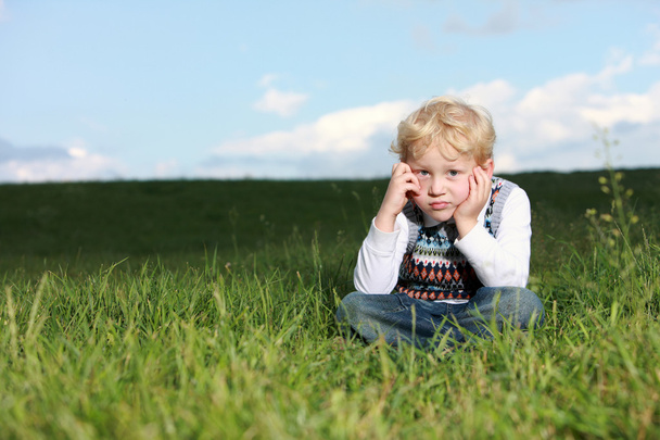 Glum little boy sitting in grass - Foto, imagen