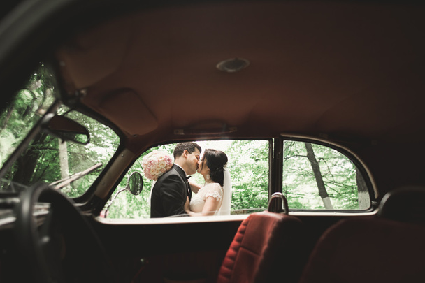 Beautiful newlywed couple posing near retro black car - Fotó, kép