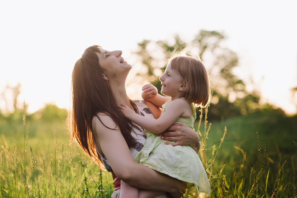 Μαμά φιλιά και αγκαλιές κόρη στην φύση σε sunsetlight - Φωτογραφία, εικόνα