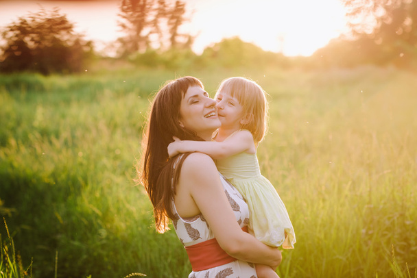 Mom kisses and hugs daughter on nature in sunsetlight - Fotoğraf, Görsel