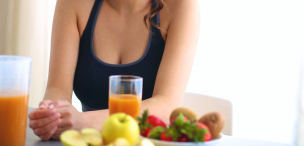 Дівчина сидить на кухні на столі з фруктами і келихами з соком
 - Фото, зображення