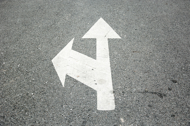 Белый двухсторонний символ со стрелкой на поверхности асфальтированной дороги
 - Фото, изображение