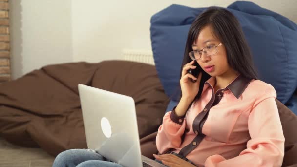 Fiatal ázsiai nő beszél a telefonon, a bab zsák széket ül - Felvétel, videó