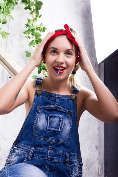 beautiful young woman in denim overalls and a bandana looking at the camera as the mirror, Chupa Chups licking and posing - Foto, imagen