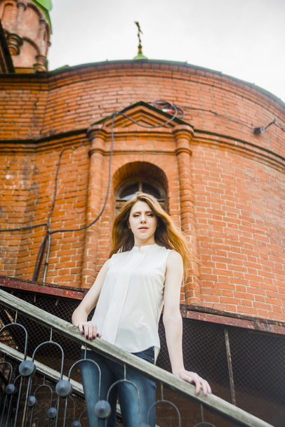 redhead young  woman standing  on stairway against old church with cross. - Foto, Imagen