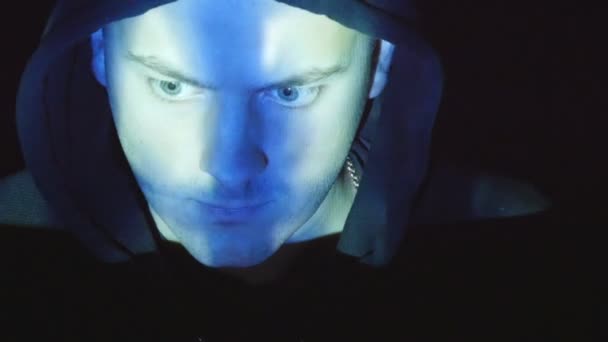 Hooded hacker working on a computer, binary code projecting on his face. Source code projected over an angry hostile mans face, black background - Footage, Video