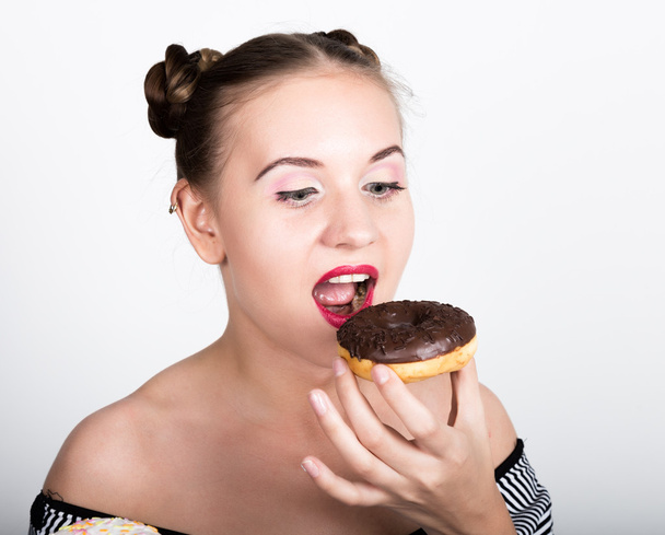 girl in bright makeup eating a tasty donut with icing. Funny joyful woman with sweets, dessert. dieting concept. junk food - Zdjęcie, obraz