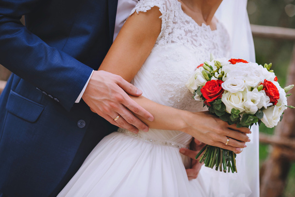 Ramo de flores rojas blancas en las manos de los recién casados
 - Foto, imagen