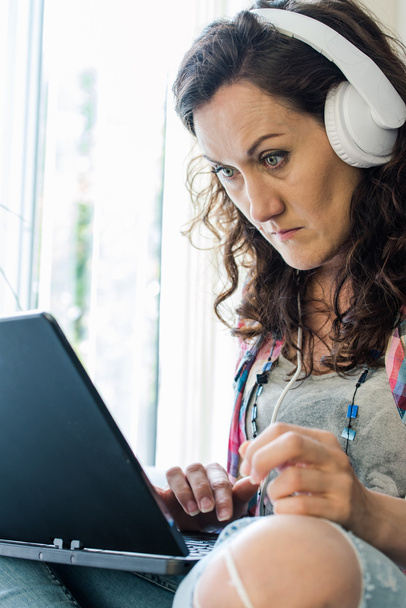 молода жінка використовує ноутбук, слухаючи музику
 - Фото, зображення