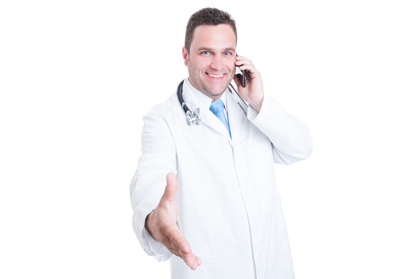 Smiling male doctor offering a handshake and speaking at phone - Foto, afbeelding