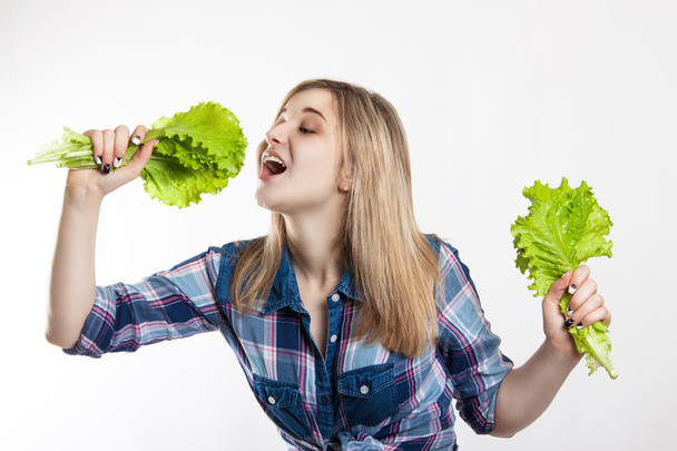 Young happy woman holding fresh green lettuce. Girl dressed in a shirt and denim shorts. Nutrition, diet, weight loss - Photo, Image