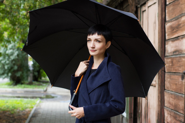 girl with an umbrella on a background of an old wooden house - Valokuva, kuva