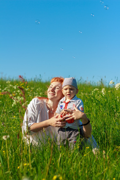 Piękna Rudowłosa matka, grając ze swoim dzieckiem w polu. - Zdjęcie, obraz