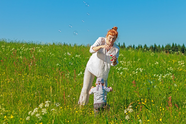 Hermosa madre pelirroja jugando con su bebé en el campo
. - Foto, Imagen