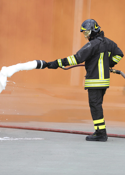 Пожарный с огнетушителем с пеной под оранжевым дымом
 - Фото, изображение