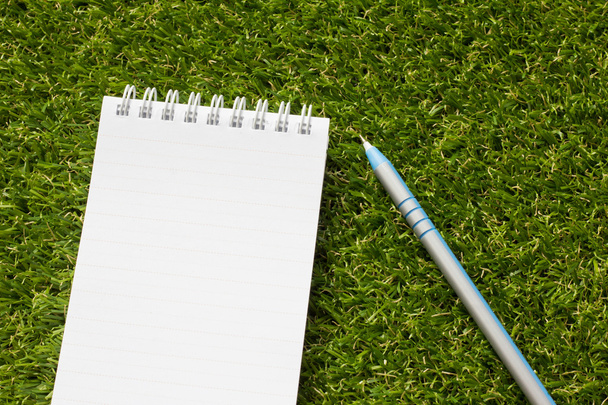 Notepad with pen on artificial green grass - Foto, imagen