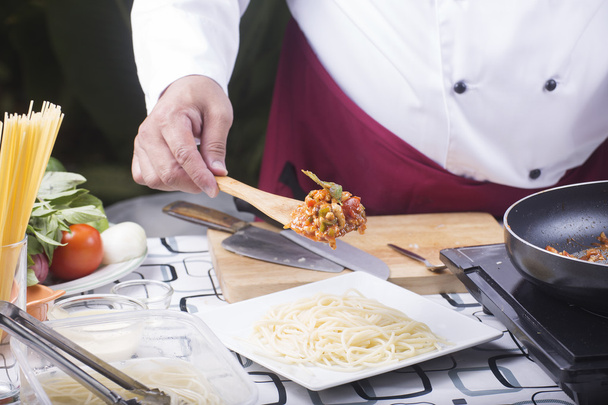 Koch legt Hühnersoße zu Spaghetti auf den Teller  - Foto, Bild