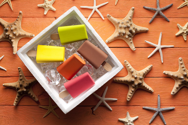Various ice lollies in thermobox and shells on wooden table - 写真・画像