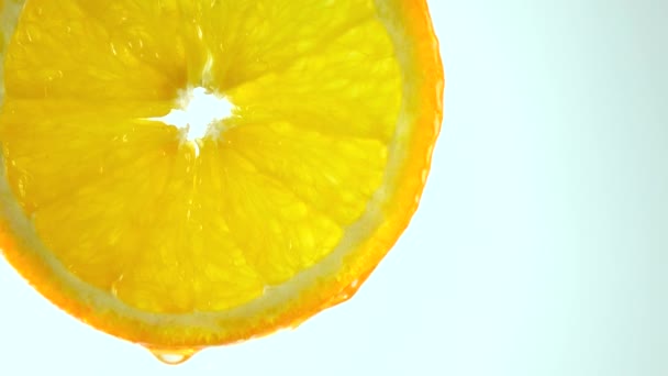 Macro 4k video van orange slice en vochtig water tegen de lichte achtergrond - Video