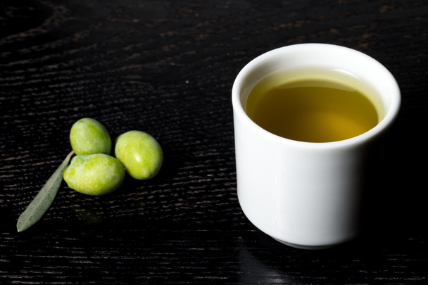 Green olive berries and cap of fresh olive oil on a black wooden - Photo, Image