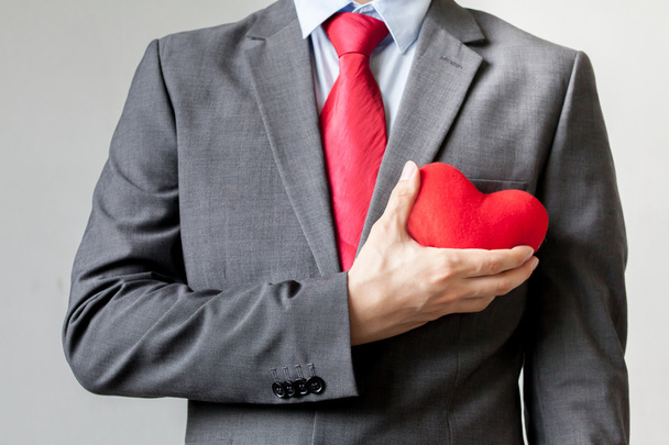 Businessman showing compassion holding red heart onto his chest in his suit - crm, service mind business concept - Foto, Bild