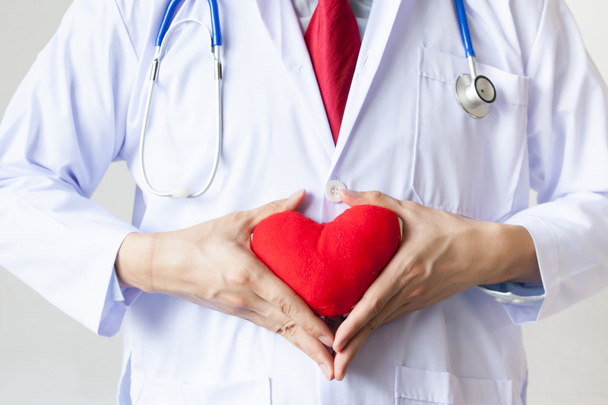 Arzt zeigt Mitgefühl und Unterstützung, indem er ein rotes Herz auf seine Brust in seinem Mantel hält - Foto, Bild