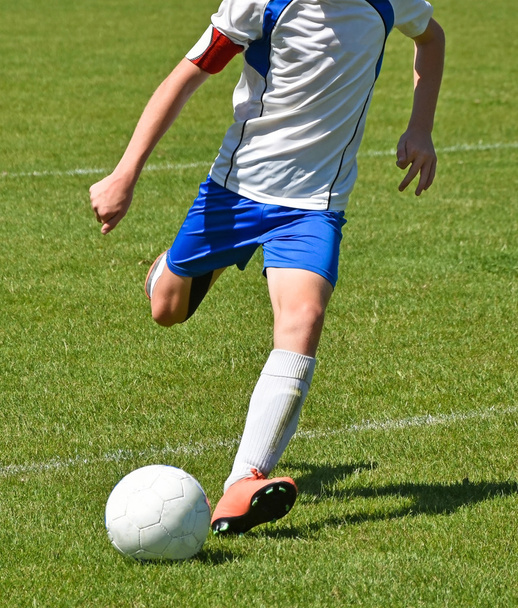 Nuori jalkapalloilija potkaisee palloa
 - Valokuva, kuva