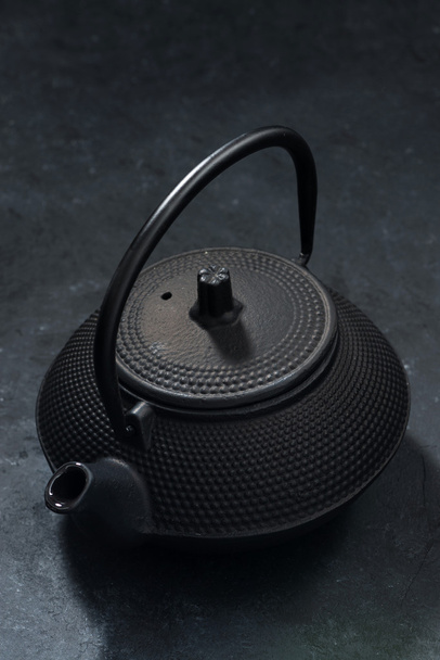Черный чугунный чайник на темном фоне, вертикальный, крупный план
 - Фото, изображение