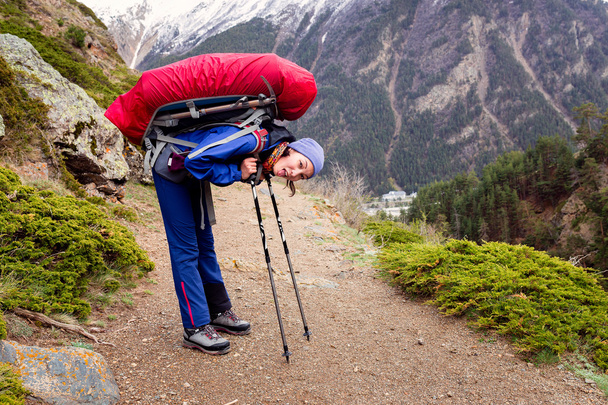 mulher caminhando com mochila ter um descanso em uma trilha com seus postes de trekking no fundo de altas montanhas do Cáucaso
 - Foto, Imagem