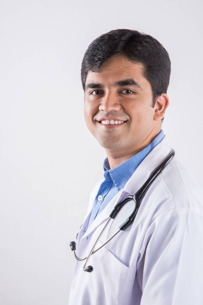 Przystojny indyjski lekarz z wesołym wyrazem twarzy i ręce złożone. stojąc na białym tle - Zdjęcie, obraz