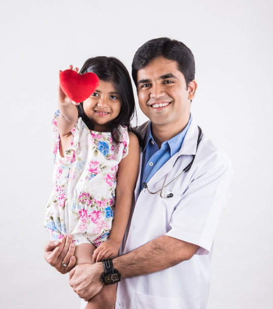 knappe pediatrische Doctor Holding een meisje van de baby, mannelijke arts met klein meisje, Indiase arts, Indiase meisje geduldig met rood hart gevulde speelgoed, hart zorgconcept en arts met meisje patiënt, geïsoleerd - Foto, afbeelding