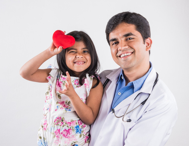 handsome pediatric doctor holding a baby girl, male doctor with small girl, indian doctor, indian girl patient with red heart stuffed toy, heart care concept and doctor with girl patient, isolated - Photo, Image