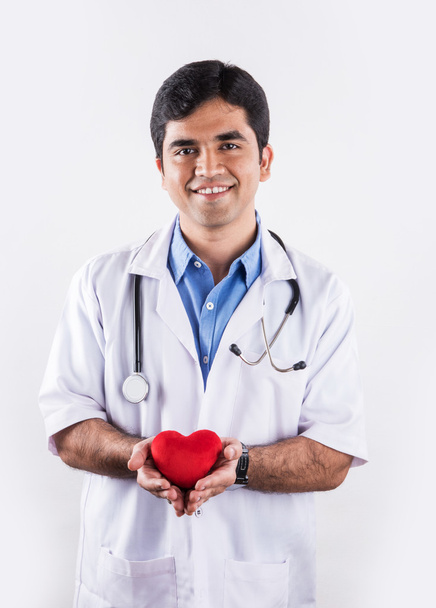 όμορφος Ινδός γιατρός κρατώντας καρδιά παραγεμισμένο παιχνίδι, γιατρός με κόκκινη καρδιά, ασιατικό γιατρό και την καρδιά φροντίδα αντίληψη, απομονωμένη σε λευκό φόντο, καρδιά στα χέρια του γιατρού - Φωτογραφία, εικόνα