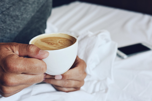 jonge man met een kopje koffie in bed - Foto, afbeelding
