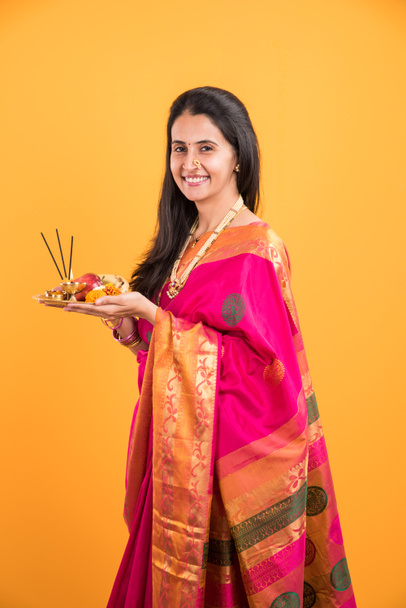 Indian woman performing puja, indian girl with pooja thali or puja thali, portrait of a beautiful young lady with pooja thali, isolated over yellow background - Photo, Image