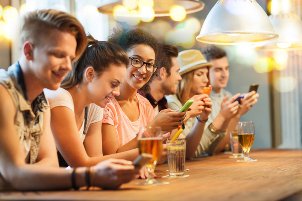 happy friends with smartphones and drinks at bar - Photo, Image