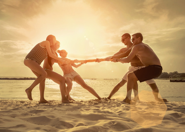 Barátok vicces húzás a háború a strandon naplemente napfény alatt. - Fotó, kép