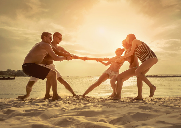 Amigos divertido tirón de la guerra en la playa bajo la luz del sol puesta del sol
. - Foto, Imagen
