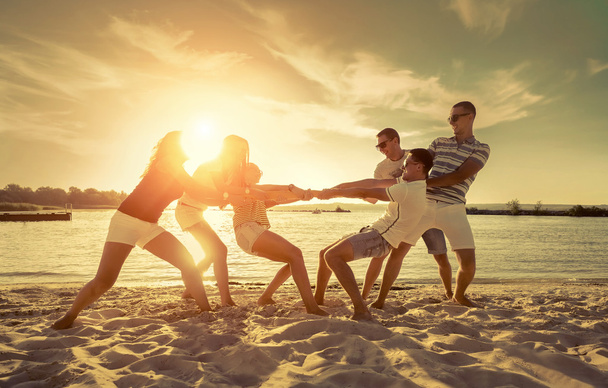 Friends funny tug of war on the beach under sunset sunlight. - Photo, Image