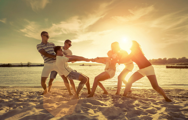 Barátok vicces húzás a háború a strandon naplemente napfény alatt. - Fotó, kép