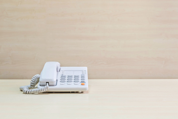 Primer plano teléfono blanco, teléfono de oficina en escritorio de madera borrosa y fondo texturizado de la pared en la sala de reuniones bajo la luz de la ventana
 - Foto, imagen