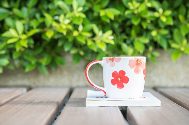 Primer plano hermosa taza de café en libro blanco en la mesa de madera borrosa y planta verde en el fondo texturizado jardín, concepto de relajación con linda taza y libro
 - Foto, Imagen