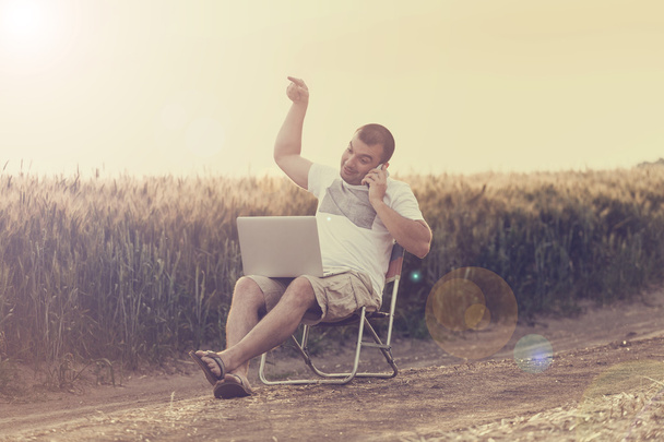 Бизнесмен, сидящий в поле и работающий над ноутбуком
. - Фото, изображение