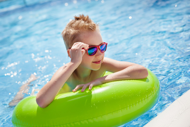 Niño nadando en la piscina con un gran anillo de goma verde brillante, divirtiéndose en el parque acuático
. - Foto, imagen