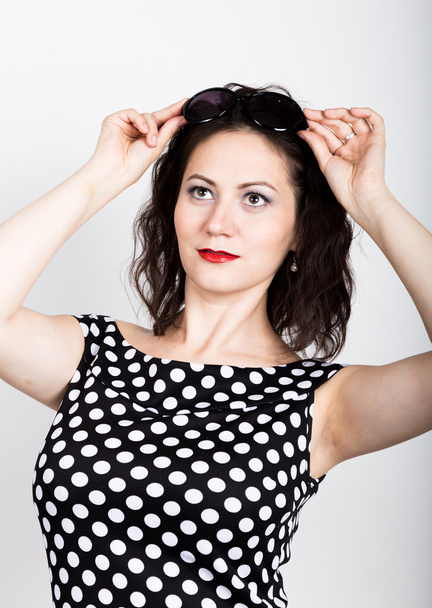 Beautiful young woman removes sun glasses, wears a dress with polka dots - Φωτογραφία, εικόνα