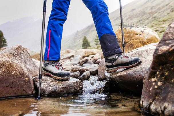 Водонепроникні трекінгові черевики пробивають скелястий гірський потік. Концепція високоякісного пішохідного обладнання
 - Фото, зображення