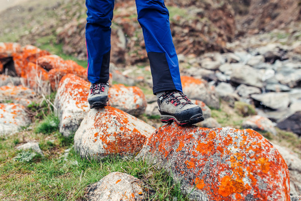 trekking and hiking boots walking on the orange lichen covered stones. Concept of quality hiking shoes - Photo, Image