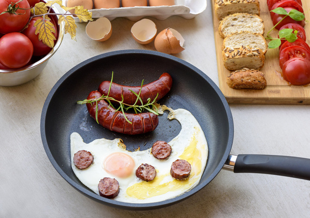 Saucisses frites et œufs dans une poêle servie avec du pain, des tomates et une coquille d'oeuf
 - Photo, image